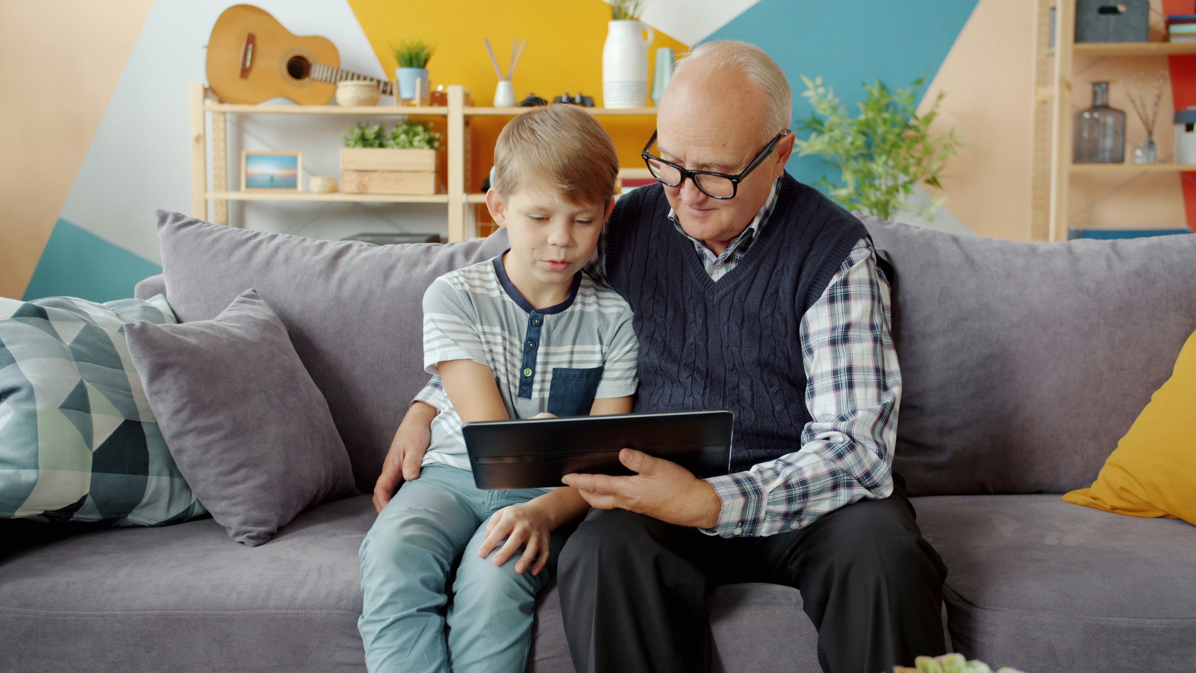 A child and a grandfather are watching the screen of the tablet