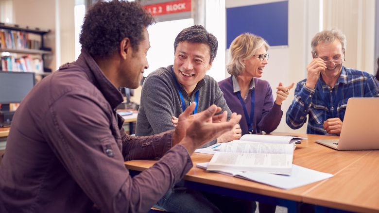 Adult learners developing literacy and digital skills with trainers, using traditional books and technology.