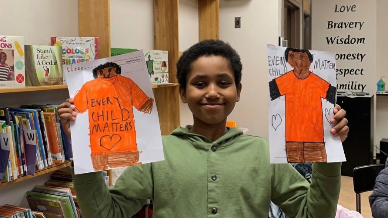 A child participating in an Indigenous reading circle, showing his drawing of orange shirts for the National Day for Truth and Reconciliation.