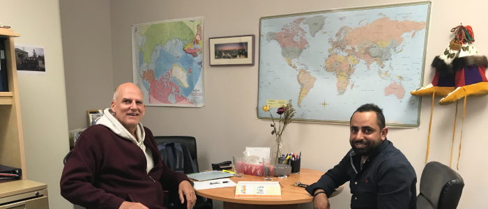 Two men sitting at a table in a room with maps on the wall