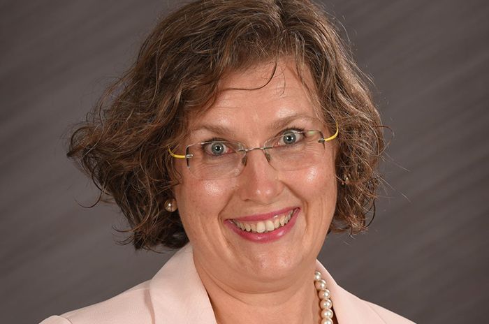 A woman with chin length brown hair and glasses. She is smiling.