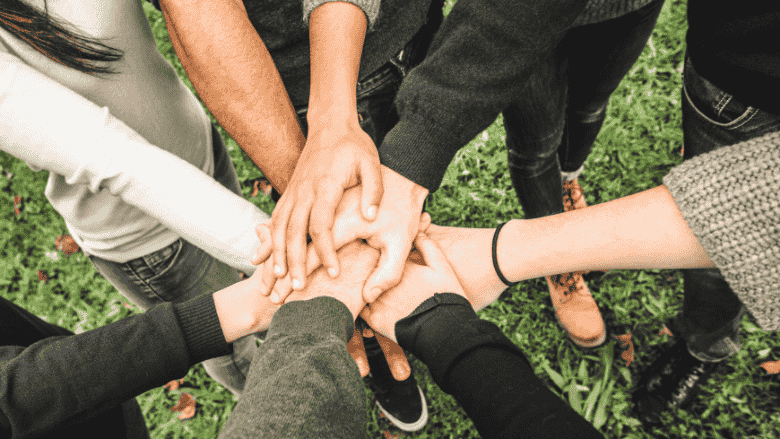 Multiple hands coming together in a unified gesture, as if preparing for a cheer or war cry, symbolizing teamwork and solidarity.