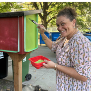 A woman is outside painting a wooden box green.
