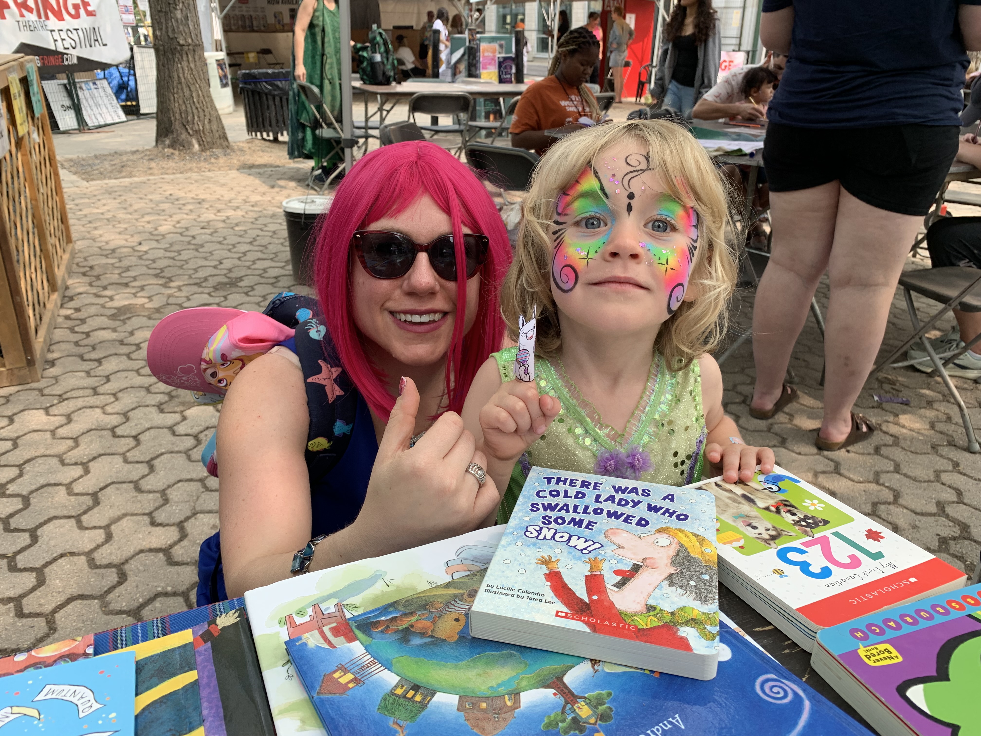 A kid and a lady with a pink wig in front of books