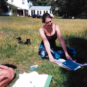 A woman sits on a lawn with books in front of her.