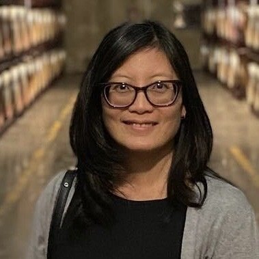 A woman with glasses and black hair smiles at the camera